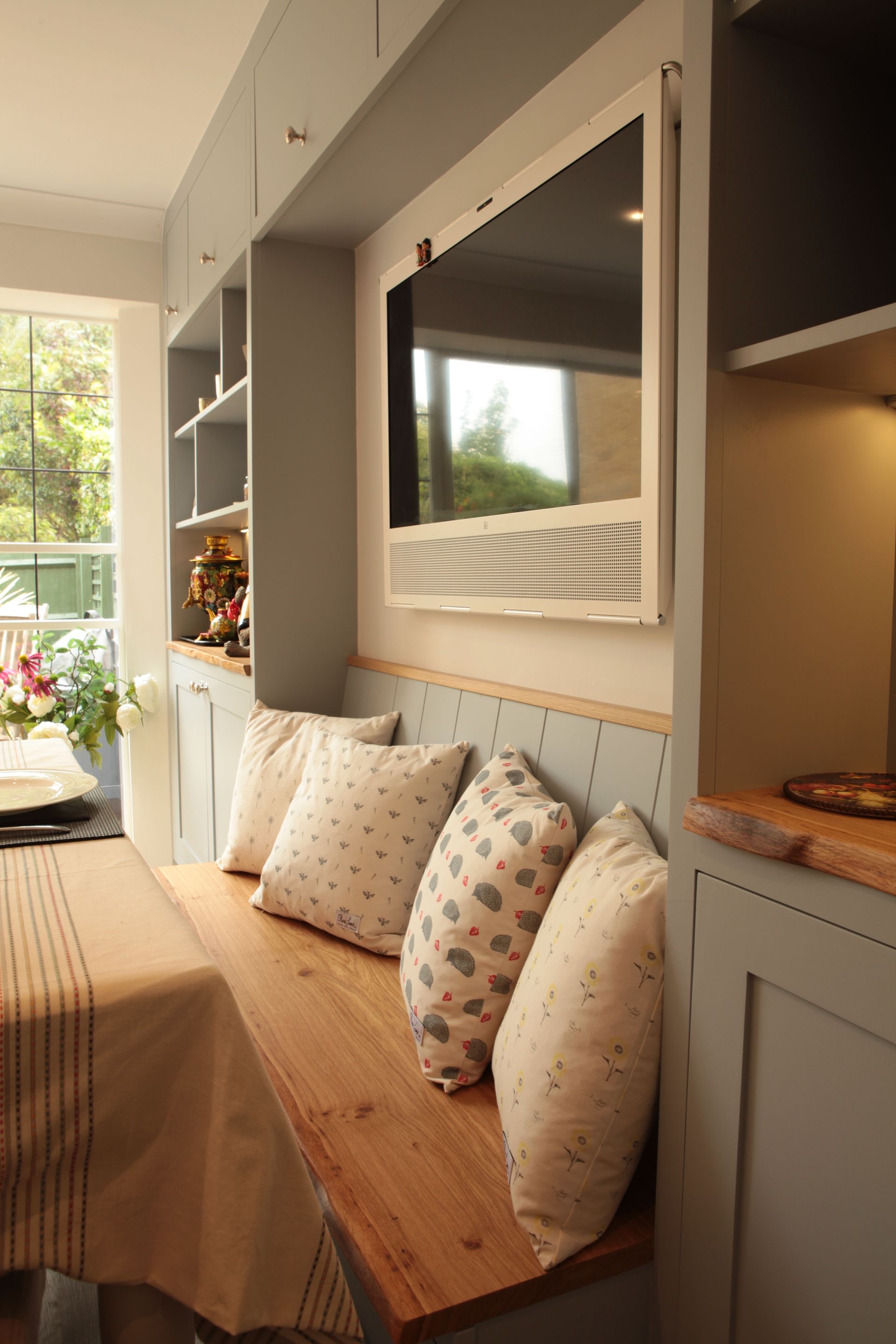 A dining room with a wooden bench and a television mounted to the wall bespoke