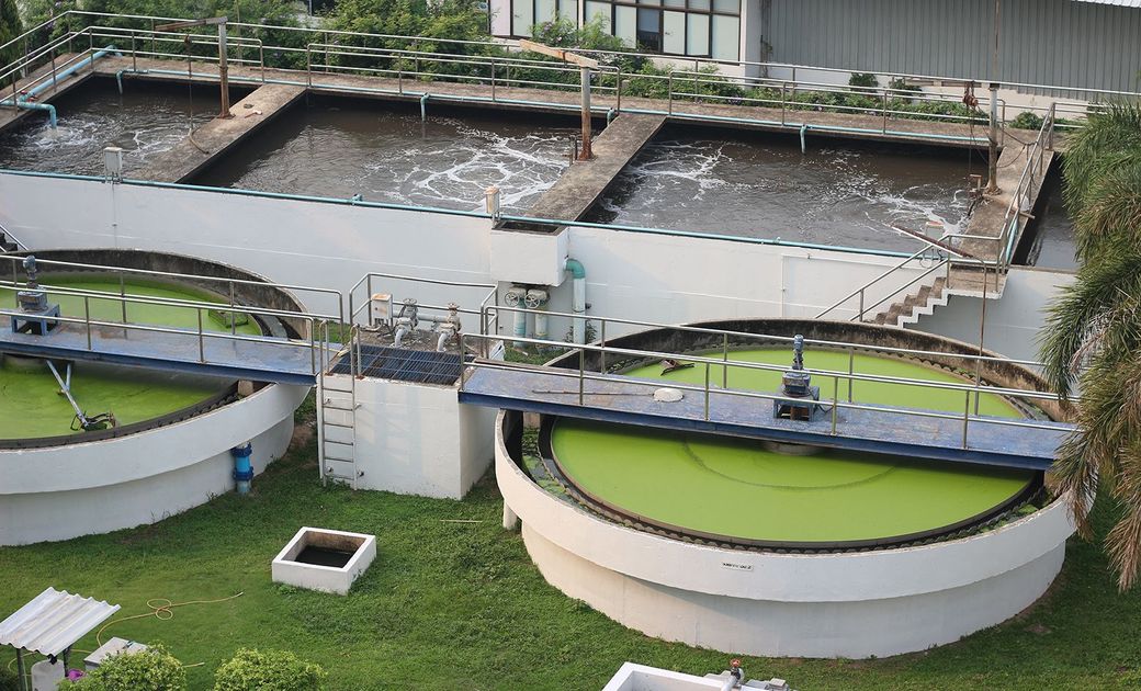 Planta de tratamiento de aguas residuales: tanques de aireación con agua burbujeante y clarificadores circulares revestidos de color verde.
