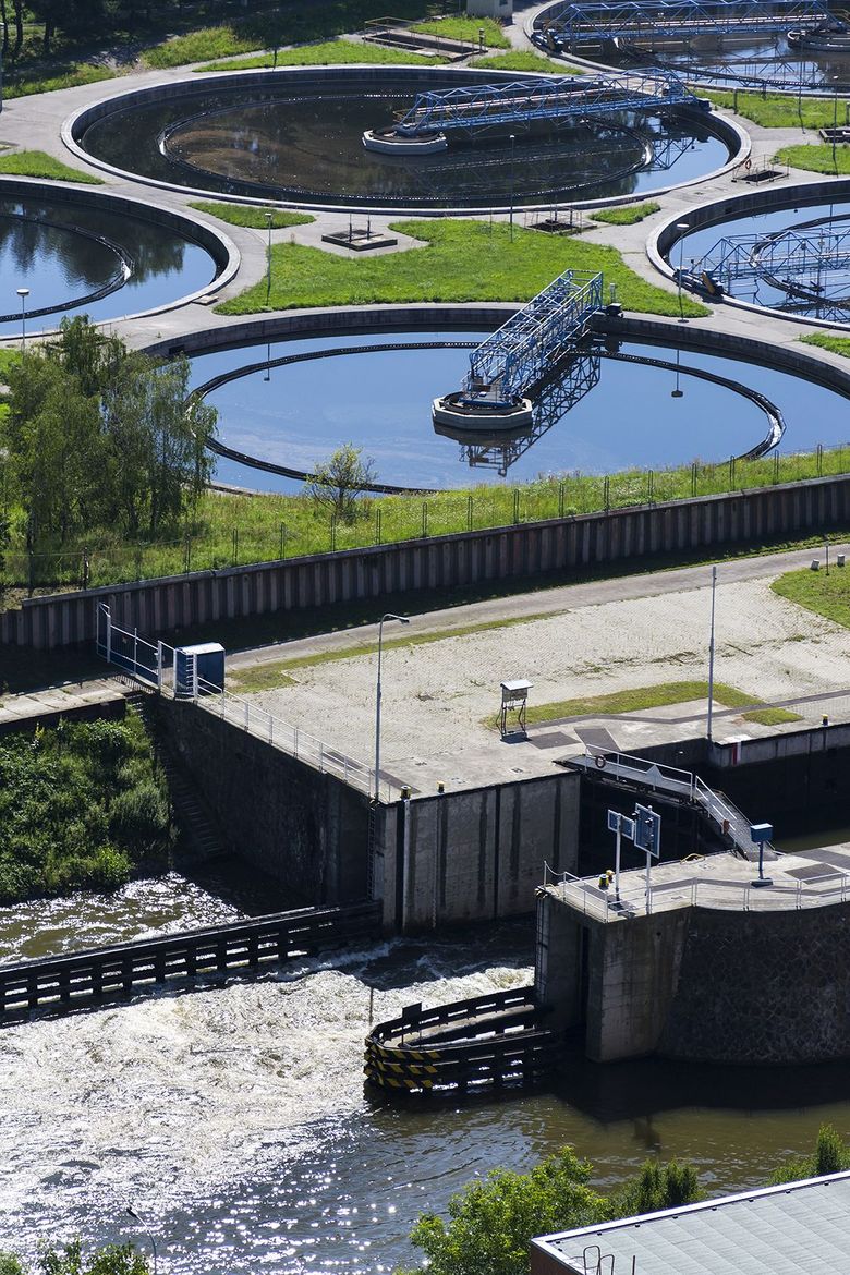 Planta de tratamiento de aguas residuales con tanques circulares y agua fluyendo a través de estructuras de concreto.