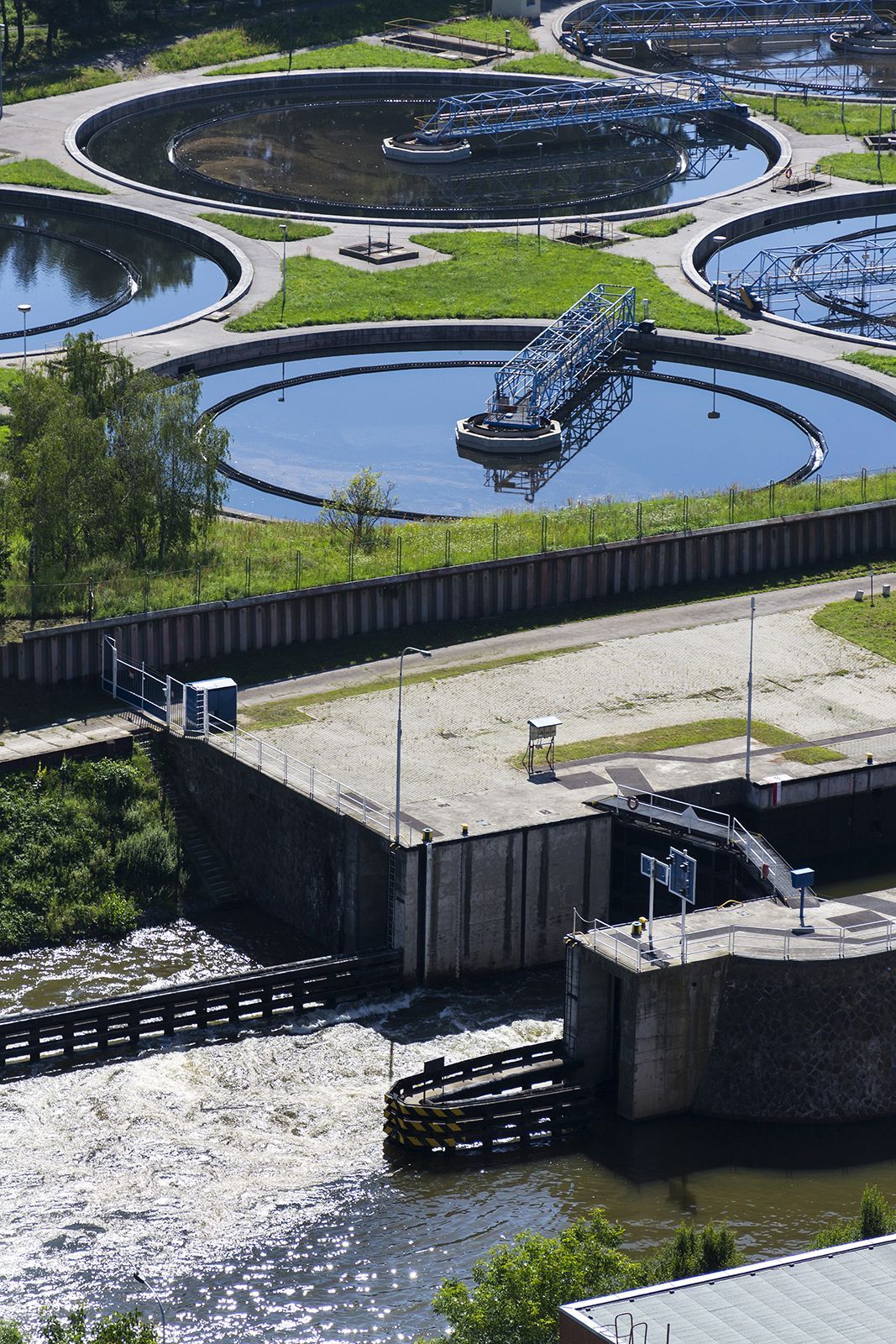 Planta de tratamiento de aguas residuales con tanques circulares y agua fluyendo a través de estructuras de concreto.