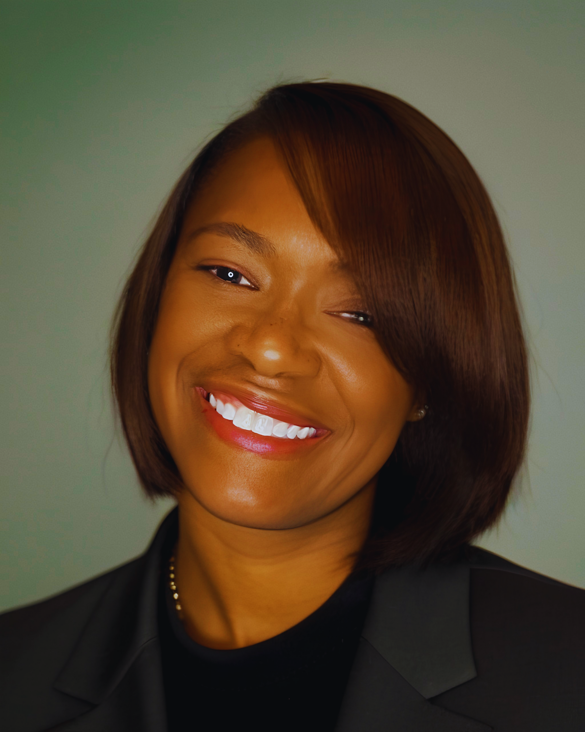 A professional portrait of a person with a bob haircut and a warm smile, wearing a dark blazer over a black top.