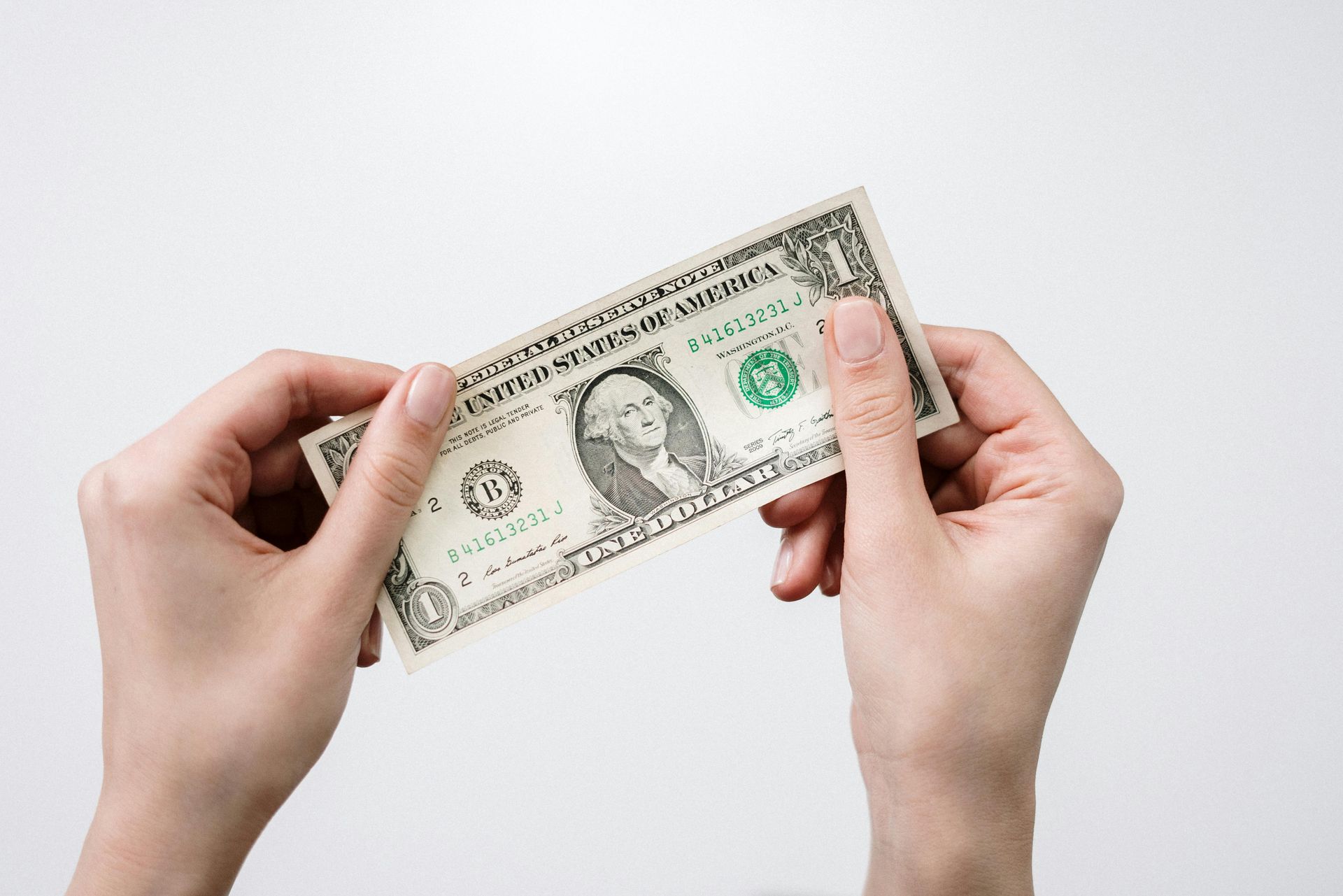 Two hands holding a one-dollar bill against a plain white background.