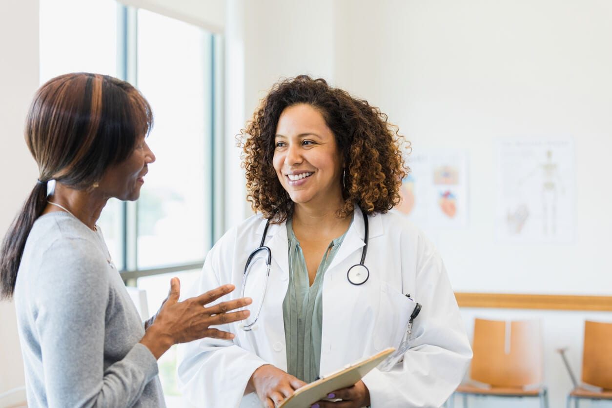 A medical professional in a white coat with a stethoscope talks to a patient in a bright, modern office.