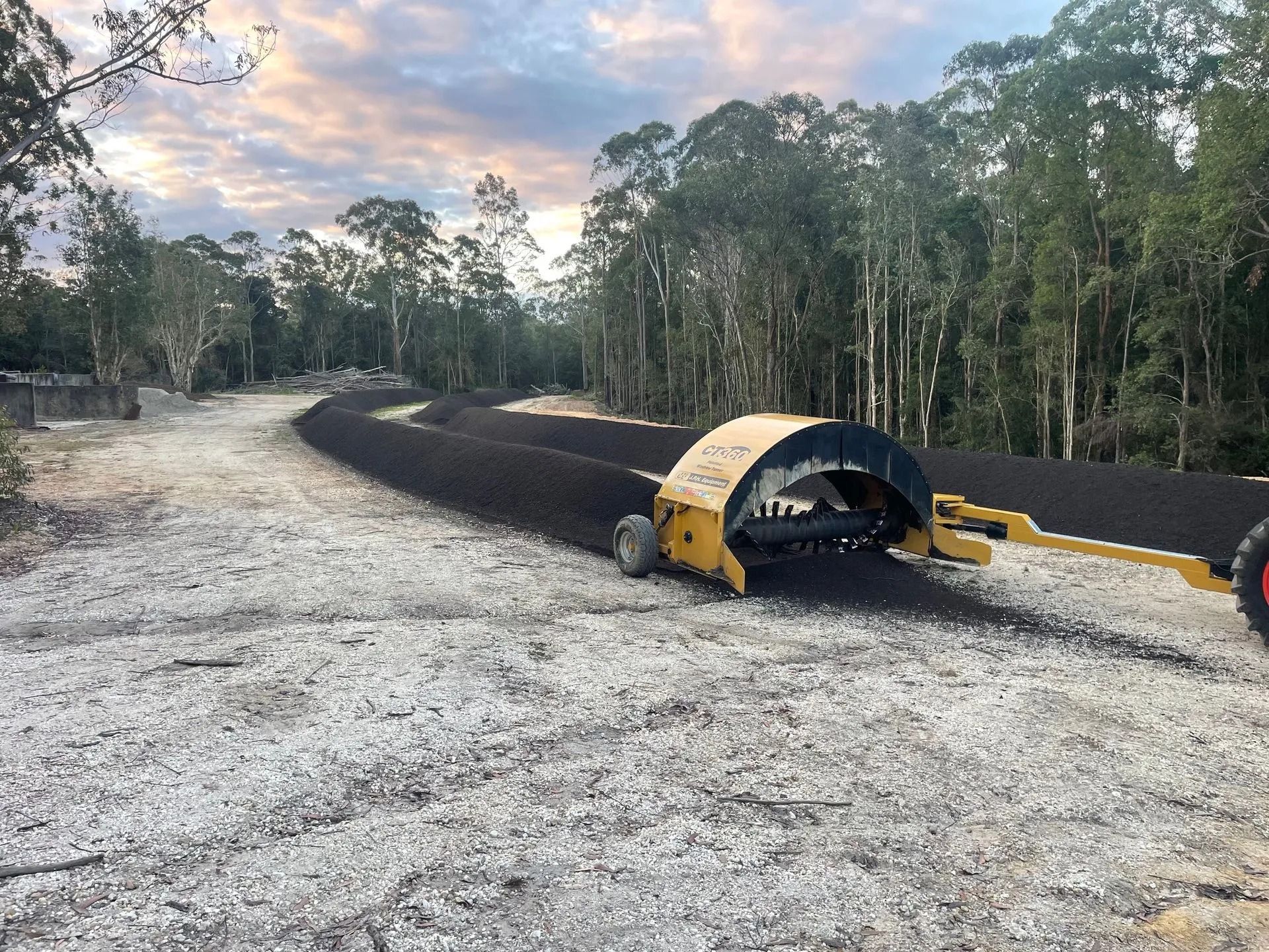 A Yellow Machine Spreads Black Material on a Gravel Road — Blue Dog Earthmoving Landscape Supplies in Newee Creek, NSW