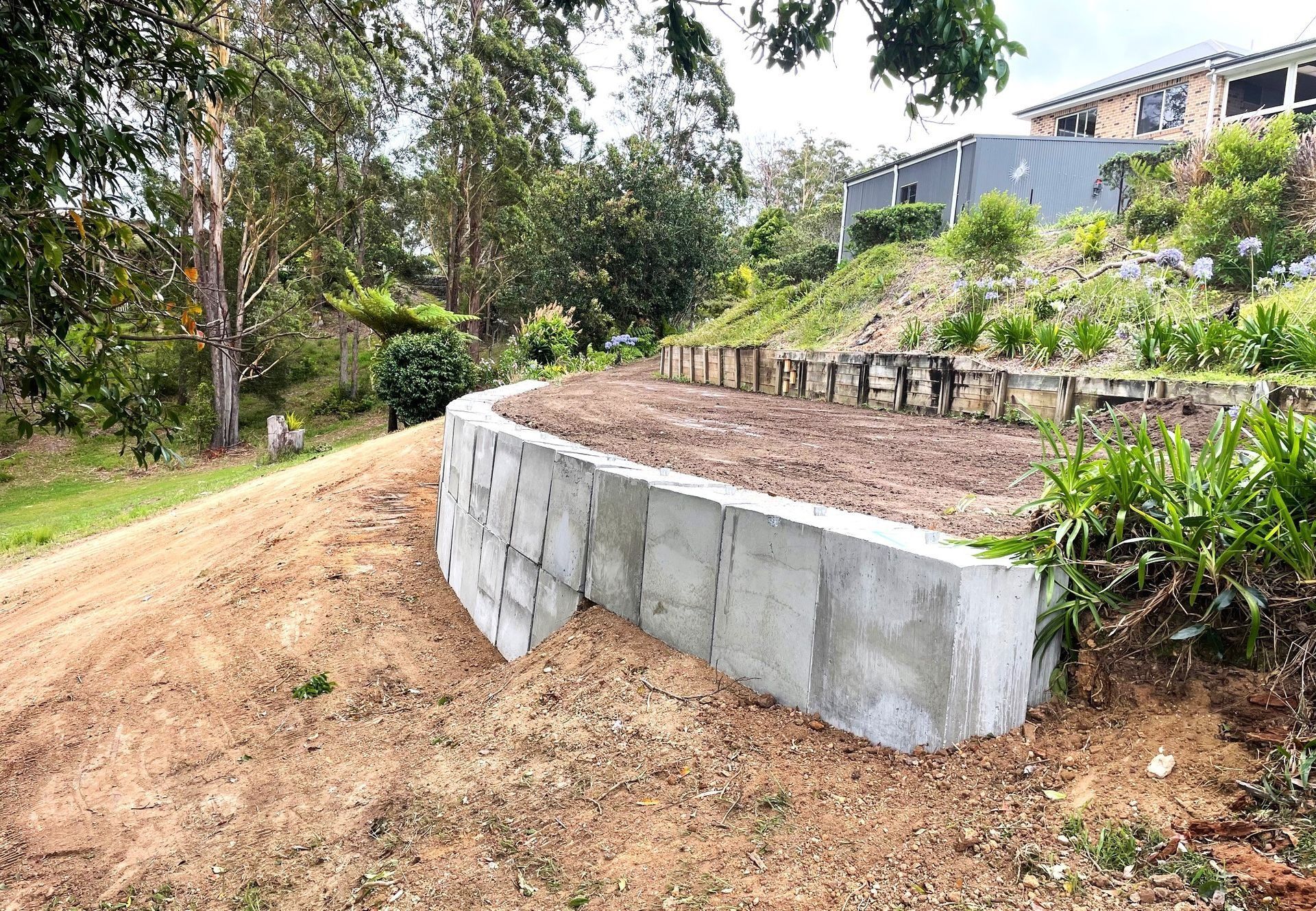 Concrete Retaining Wall on a Hillside With a Graded Dirt Area in Front — Blue Dog Earthmoving Landscape Supplies in Urunga, NSW