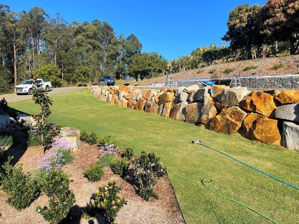 A Grassy Lawn With a Large Rock Wall, a Road — Blue Dog Earthmoving Landscape Supplies in Newee Creek, NSW