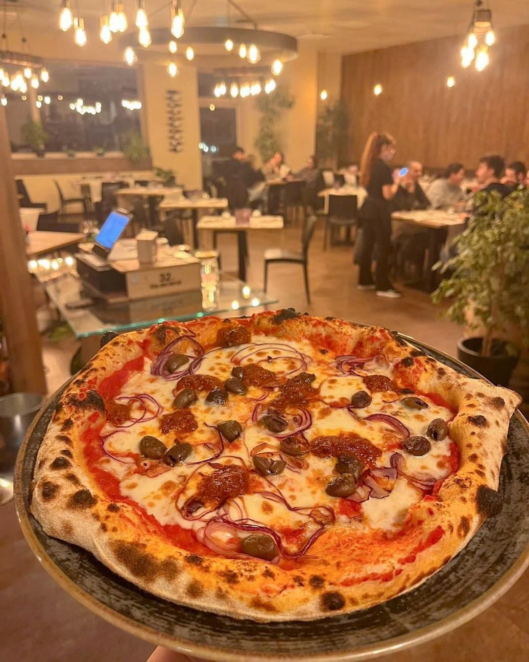 Una persona tiene in mano una pizza su un piatto in un ristorante.