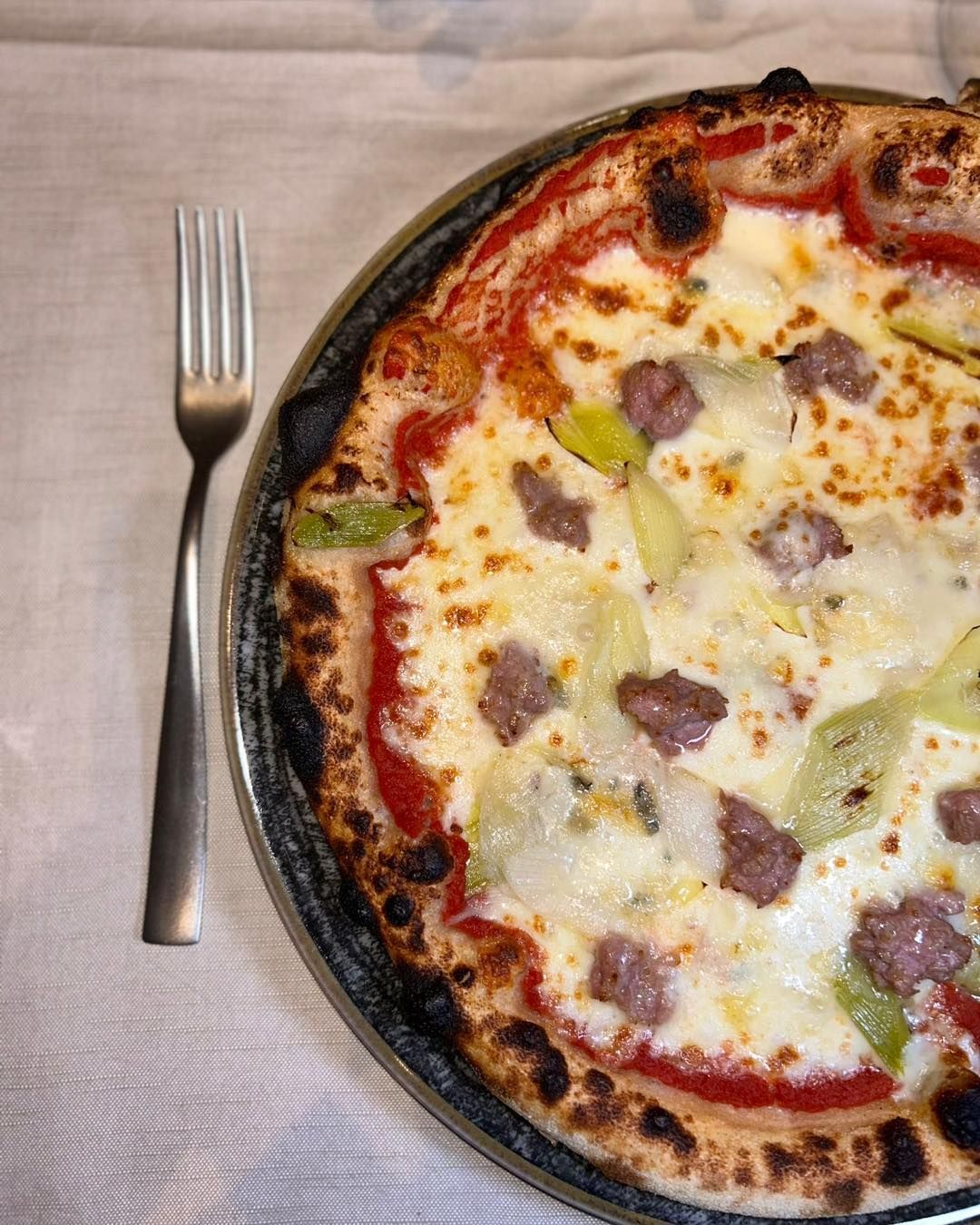 Una pizza è appoggiata su un piatto accanto a una forchetta.