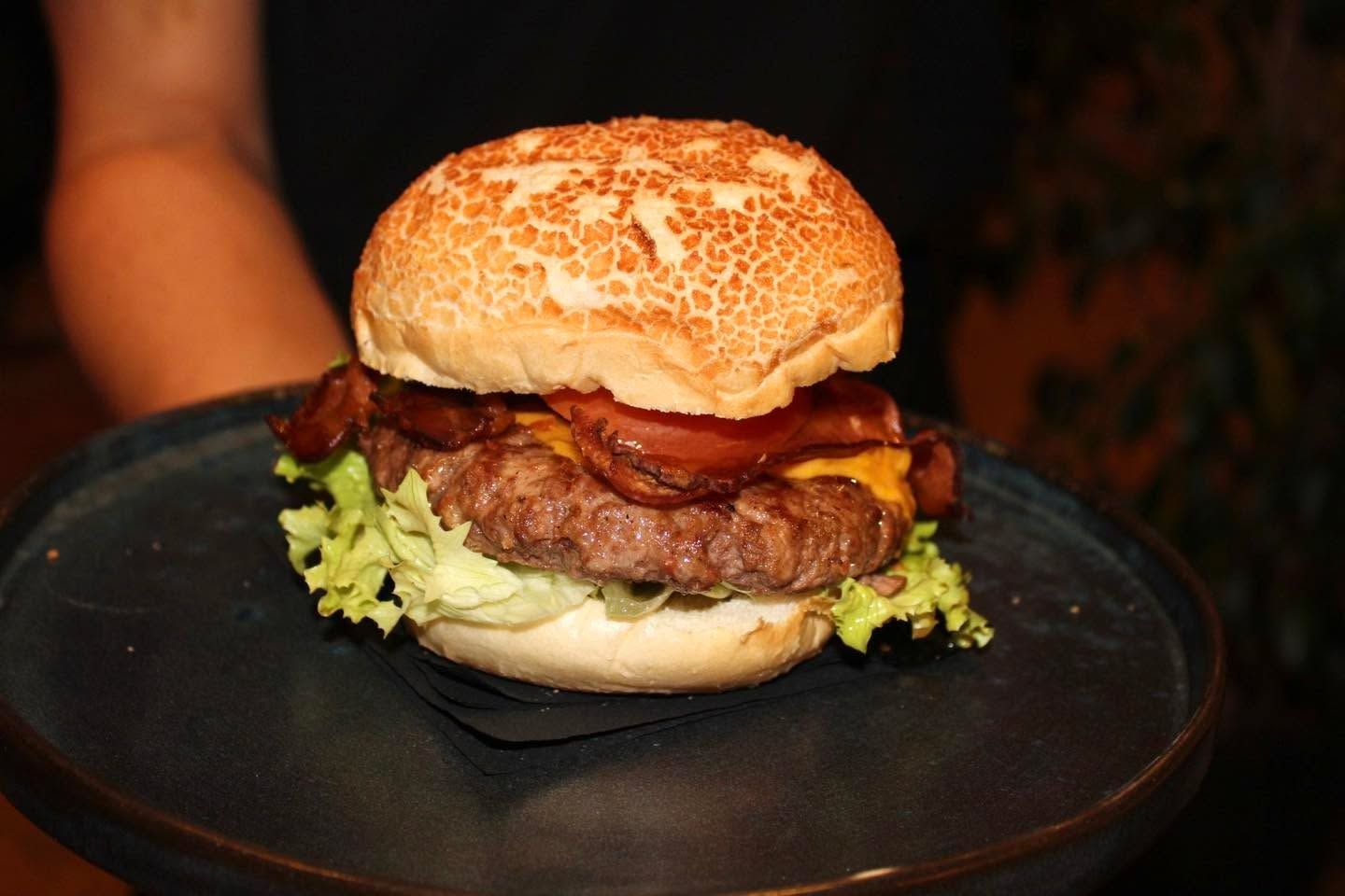 Una persona tiene in mano un piatto nero con un hamburger sopra.