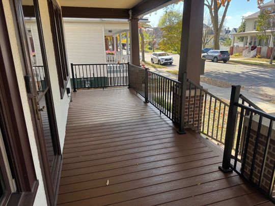 A wooden deck with steps in a backyard with autumn trees and houses in the background.