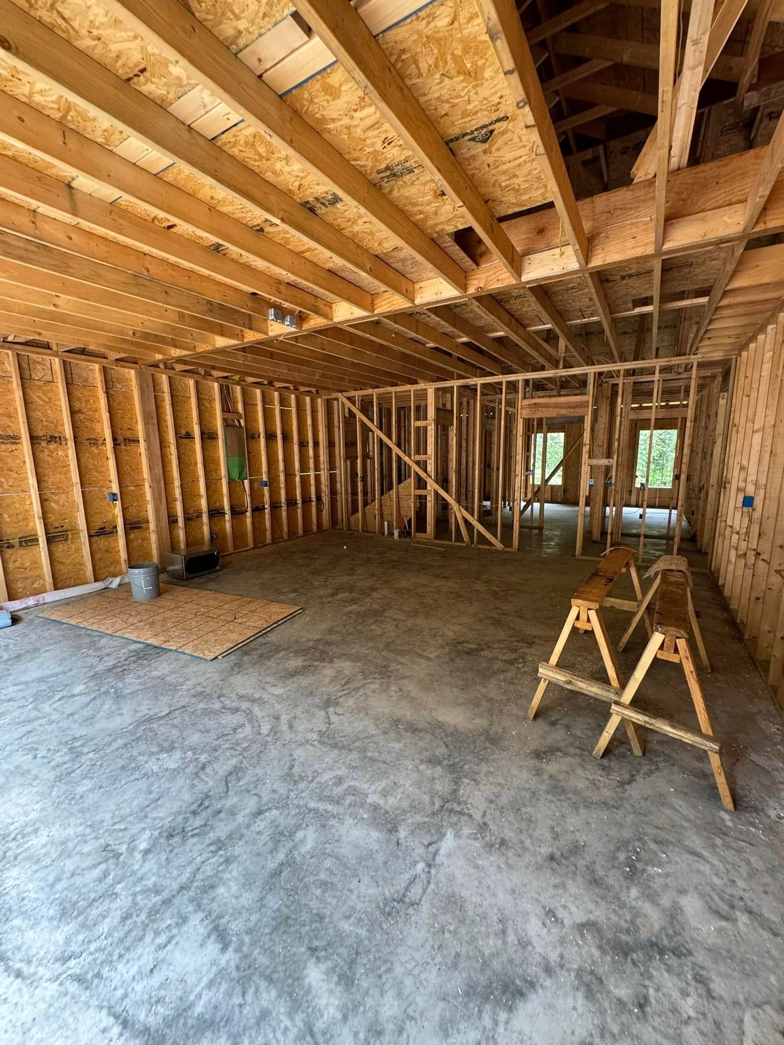 Interior of a house under construction. Bare wooden framing of walls and ceiling, concrete floor. Two wooden sawhorse supports sit in the foreground.