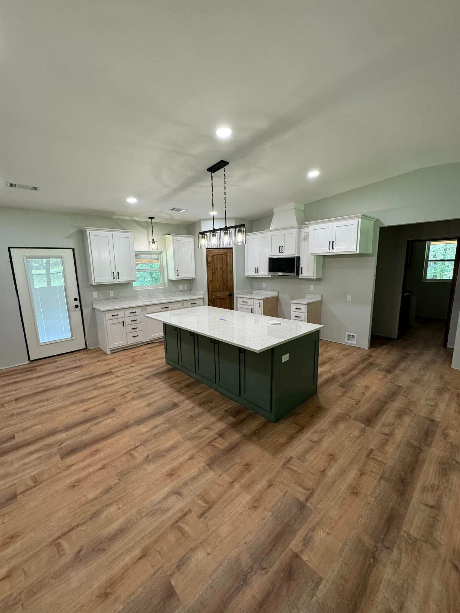 Newly renovated kitchen with white cabinets, a green island, and wood-look flooring. Natural light streams in, creating a bright, open space.