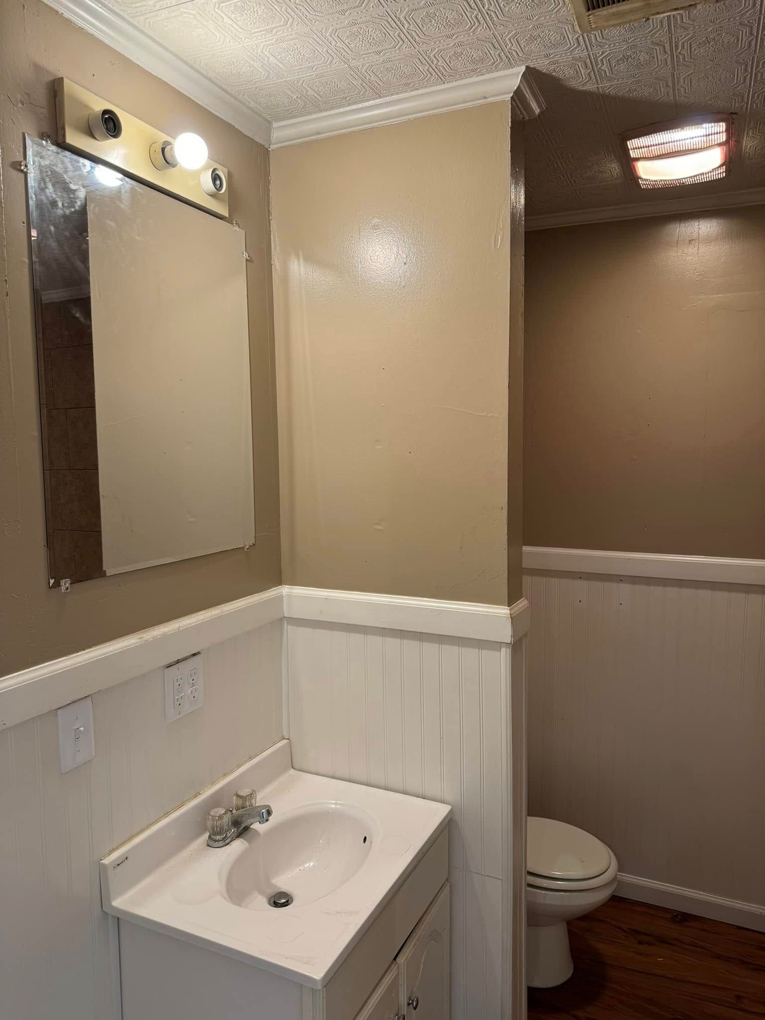 A small bathroom with a white sink, toilet, and wainscoting. The walls are tan and the ceiling is textured.