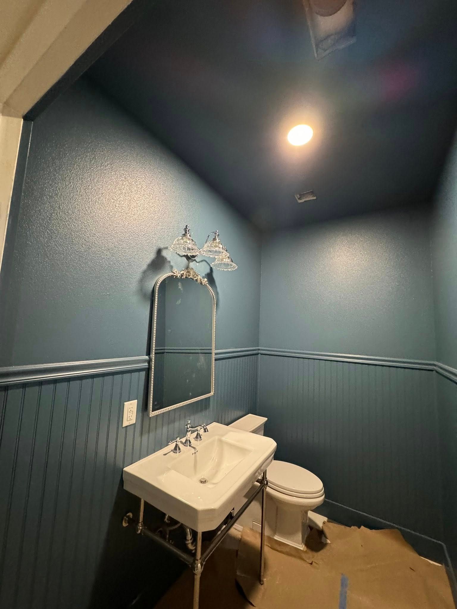 Small blue powder room with a pedestal sink, toilet, and ornate mirror. Walls have a textured, speckled effect.
