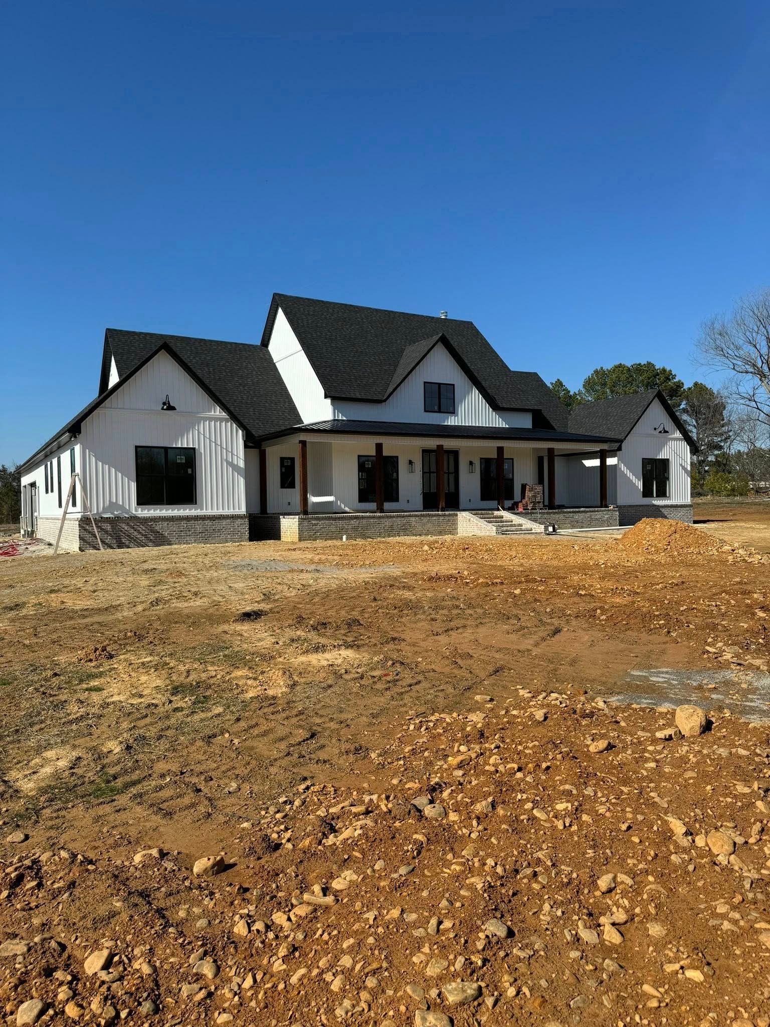 Modern farmhouse under construction with white siding, black trim, and a dark roof against a blue sky.