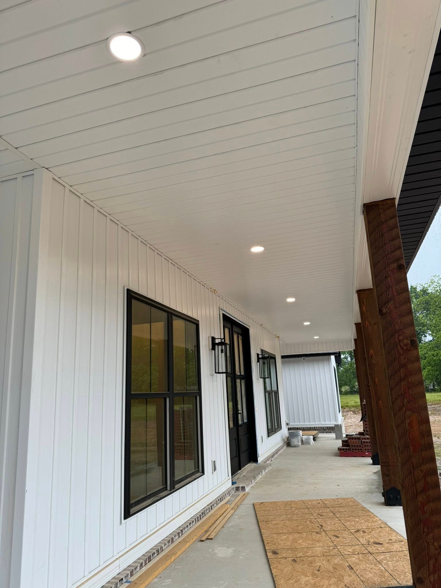 A porch exterior with white siding, a white ceiling with recessed lights, and black-framed windows and doors.