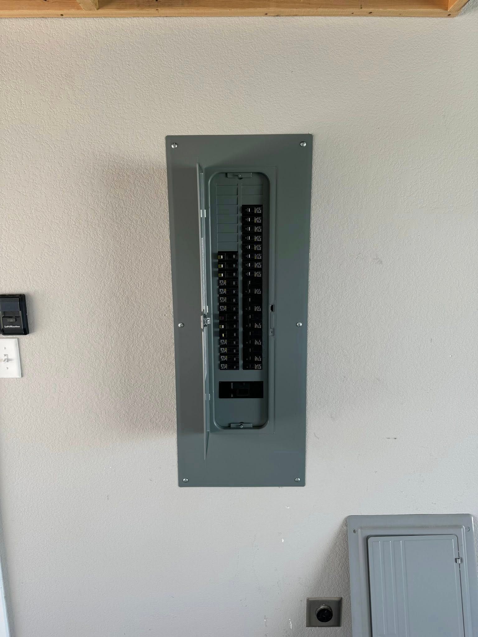 Electrical panel mounted on a textured gray wall. The panel's door is open, revealing a row of circuit breakers.