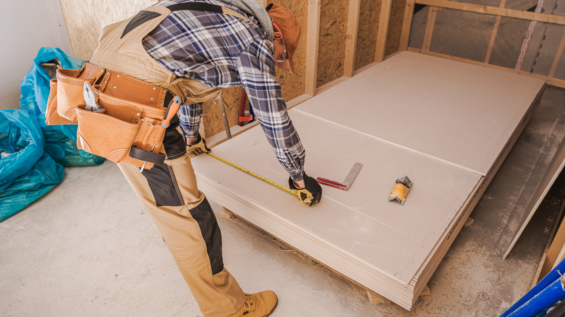 A man is measuring a piece of drywall with a tape measure.
