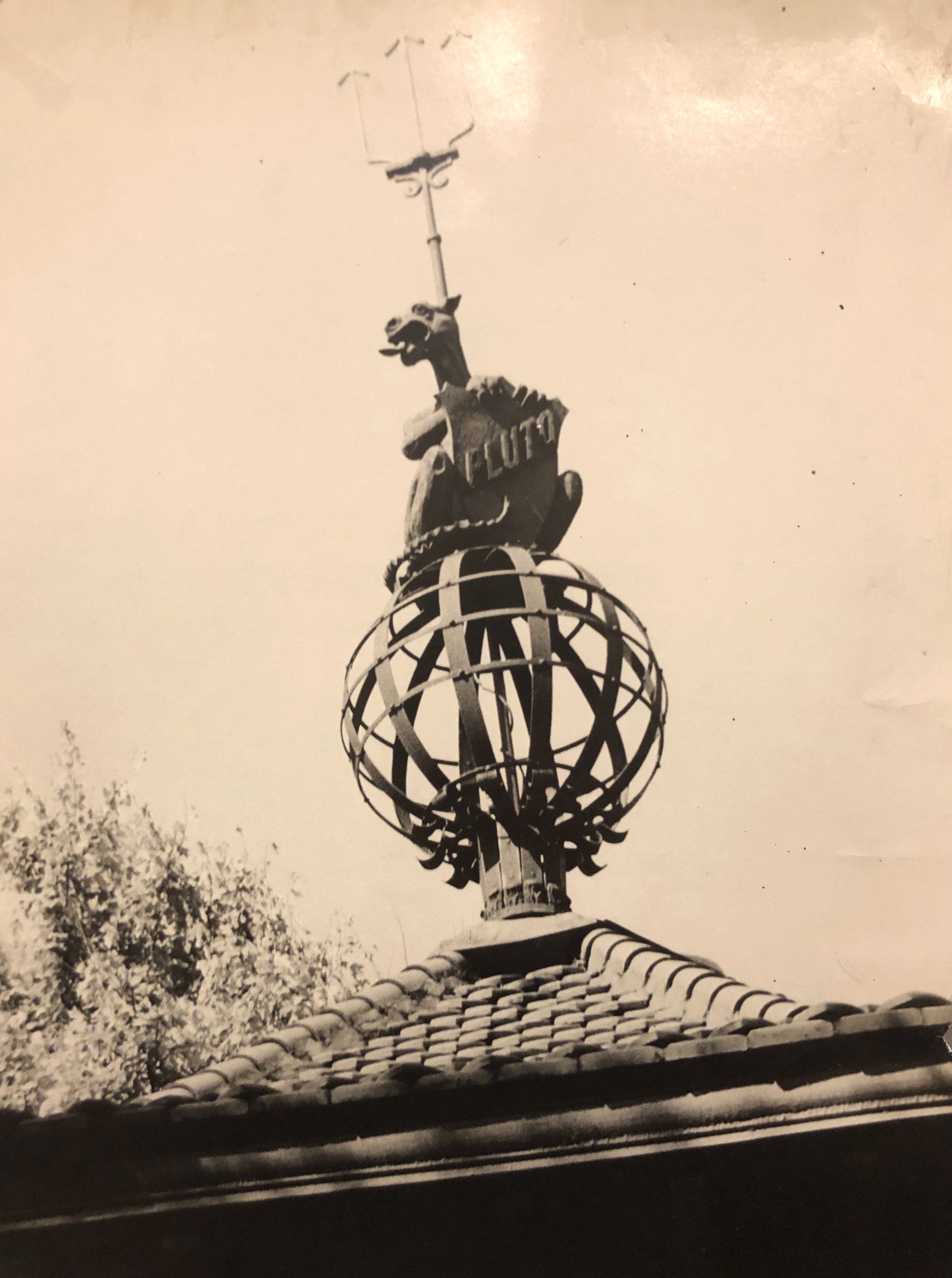 A black and white photo of Pluto weather vane on top of a building