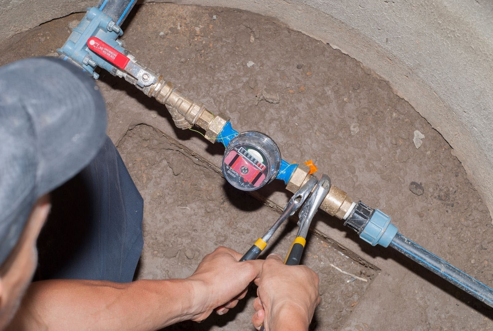 A man is fixing a water meter with pliers.