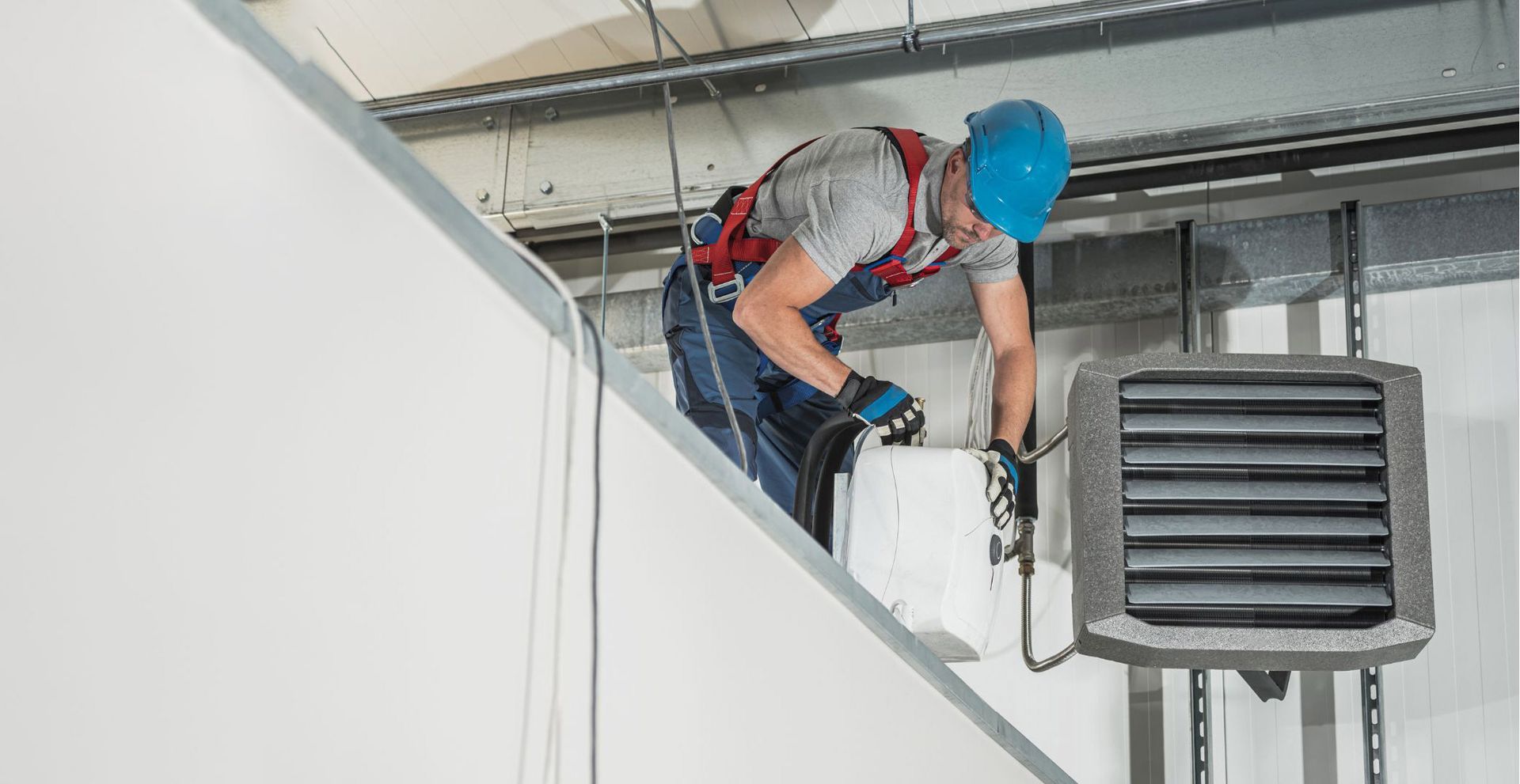 A man is working on a heater on the ceiling of a building.