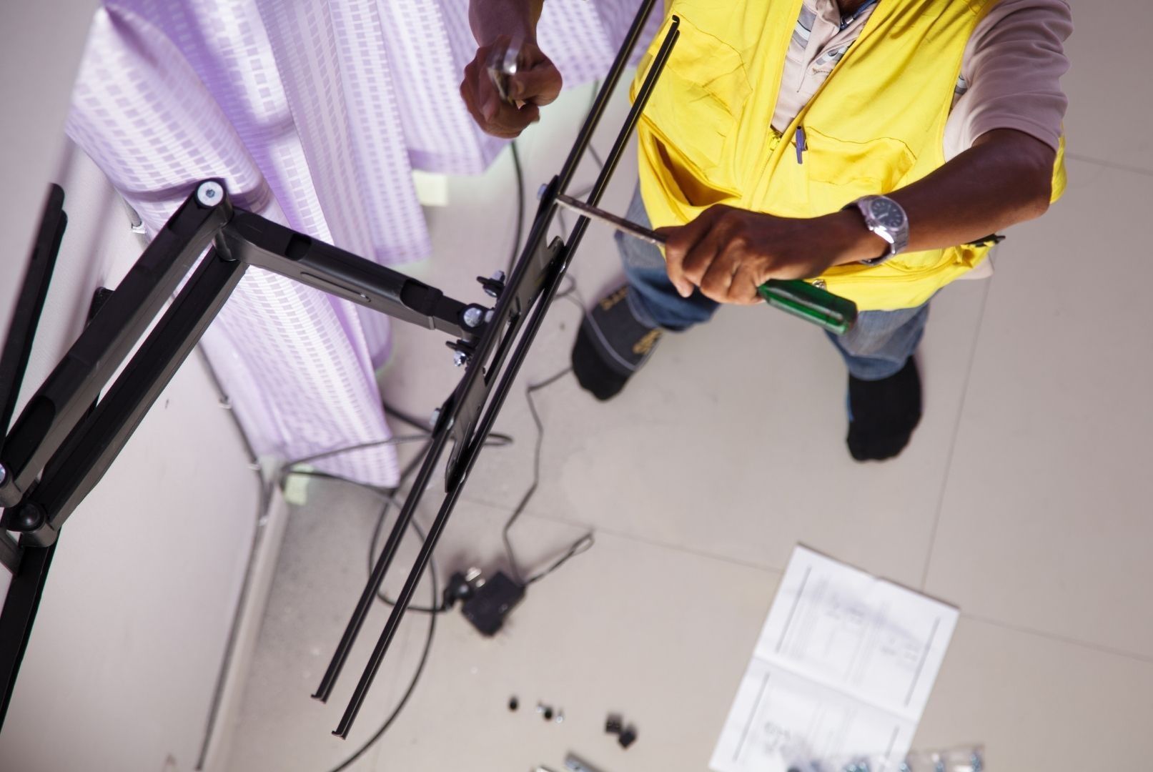 A man in a yellow vest is working on a television mount.
