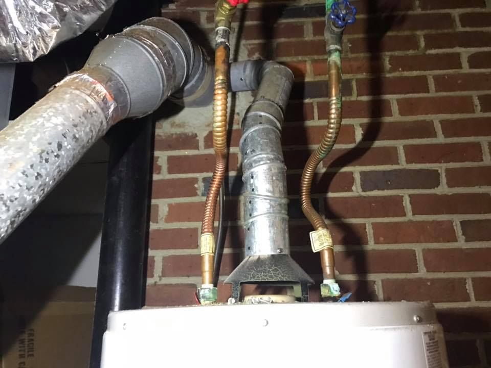 A water heater is attached to a brick wall with pipes coming out of it.