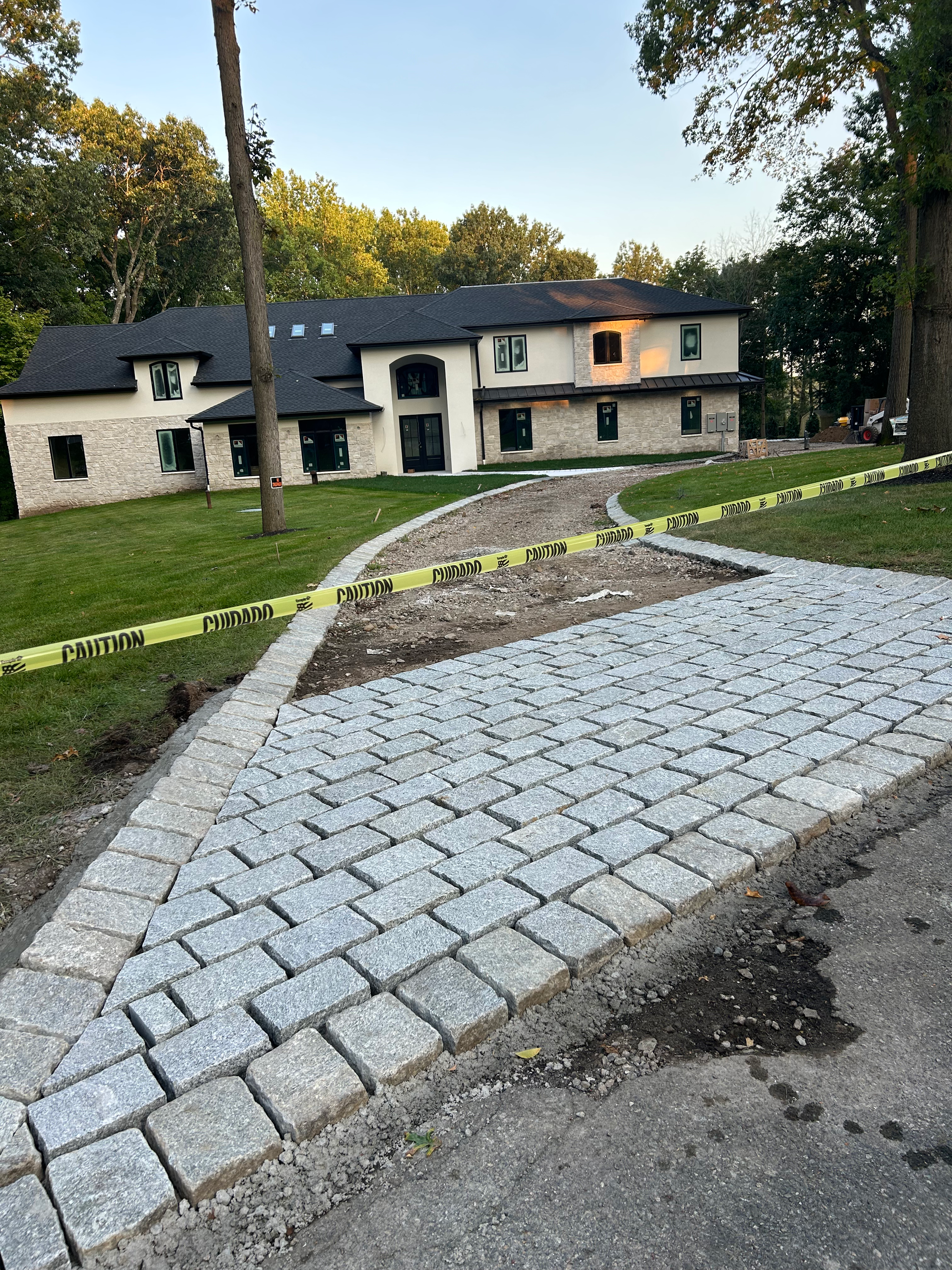 Driveway under construction with gray pavers leading to a two-story house with light-colored siding.