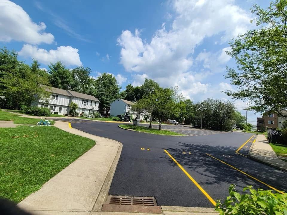 Yellow asphalt paving machine dispensing a pile of dark asphalt onto a road surface.