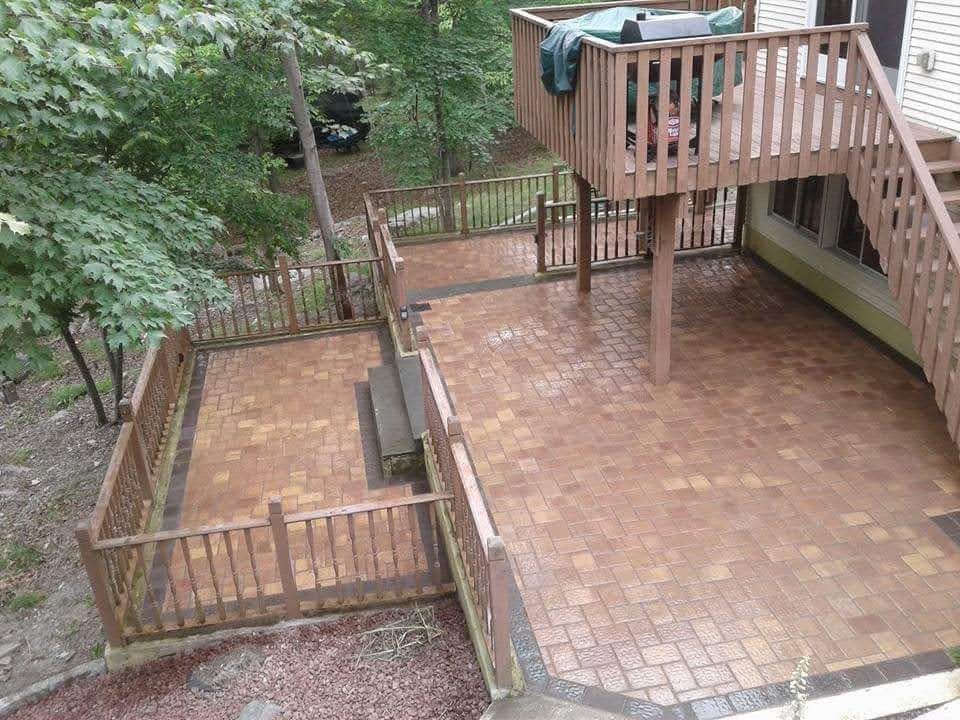 Brick patio with wooden deck and railings in a wooded setting.
