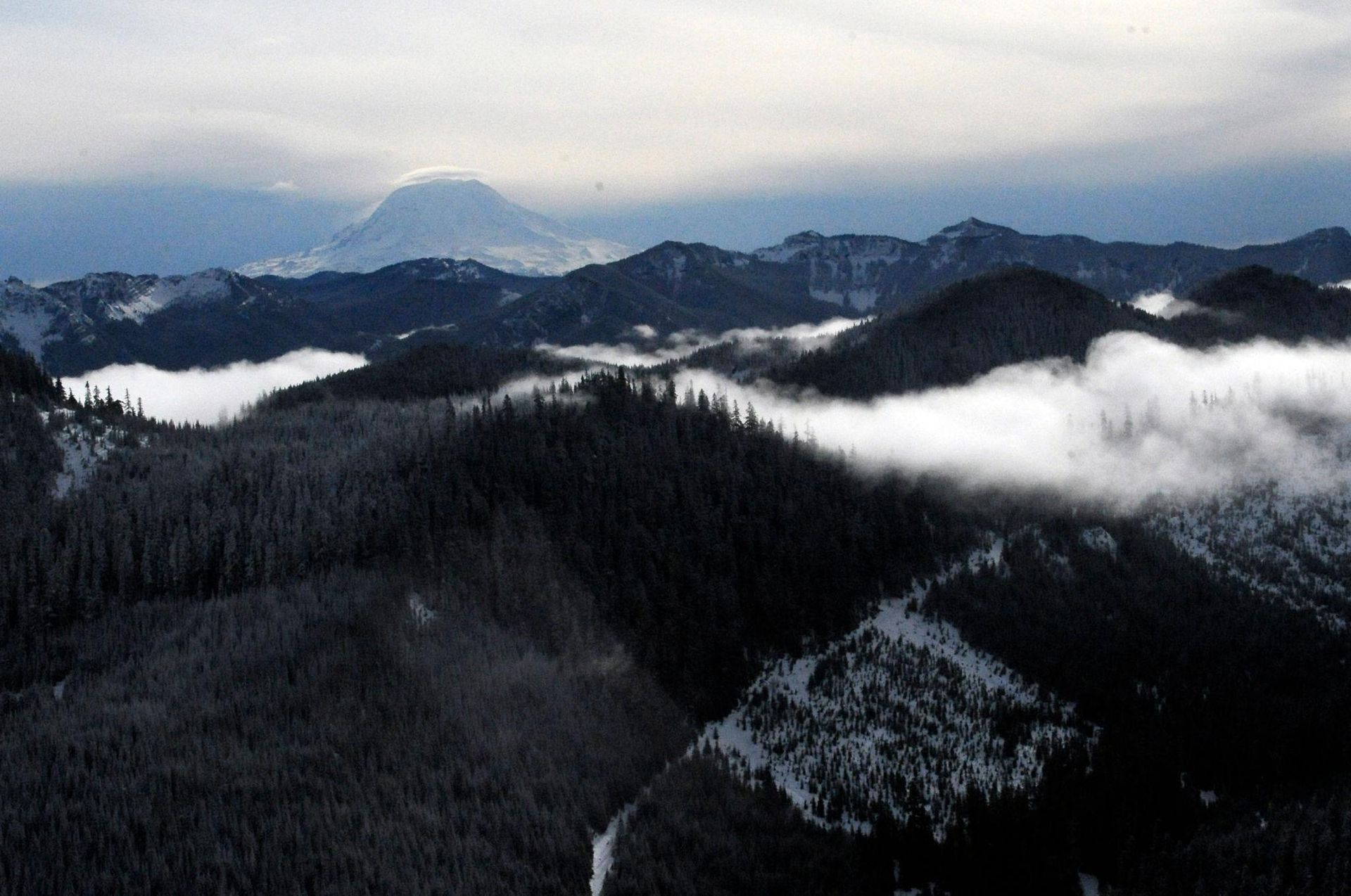 Snow-covered mountain range with a distant, snow-capped peak and low-lying clouds.