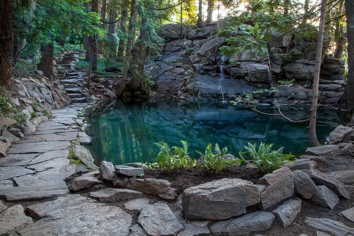 Stone pathway leads to a clear turquoise pond surrounded by rocks and trees.