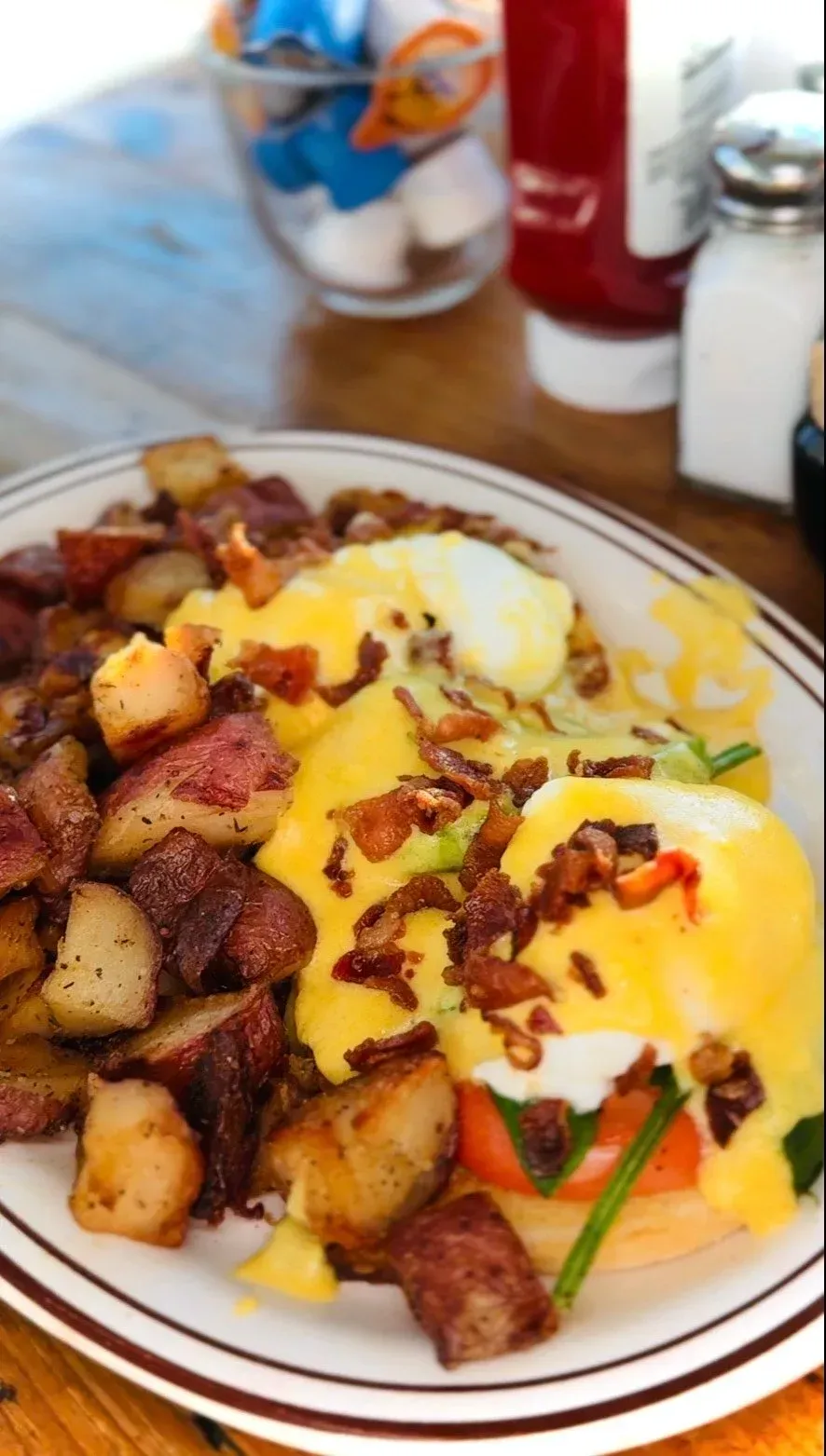 Eggs Benedict with fried potatoes. Poached eggs with hollandaise sauce, bacon, on a plate.