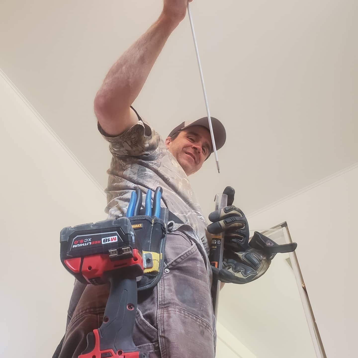 A man is standing on a ladder holding a screwdriver.