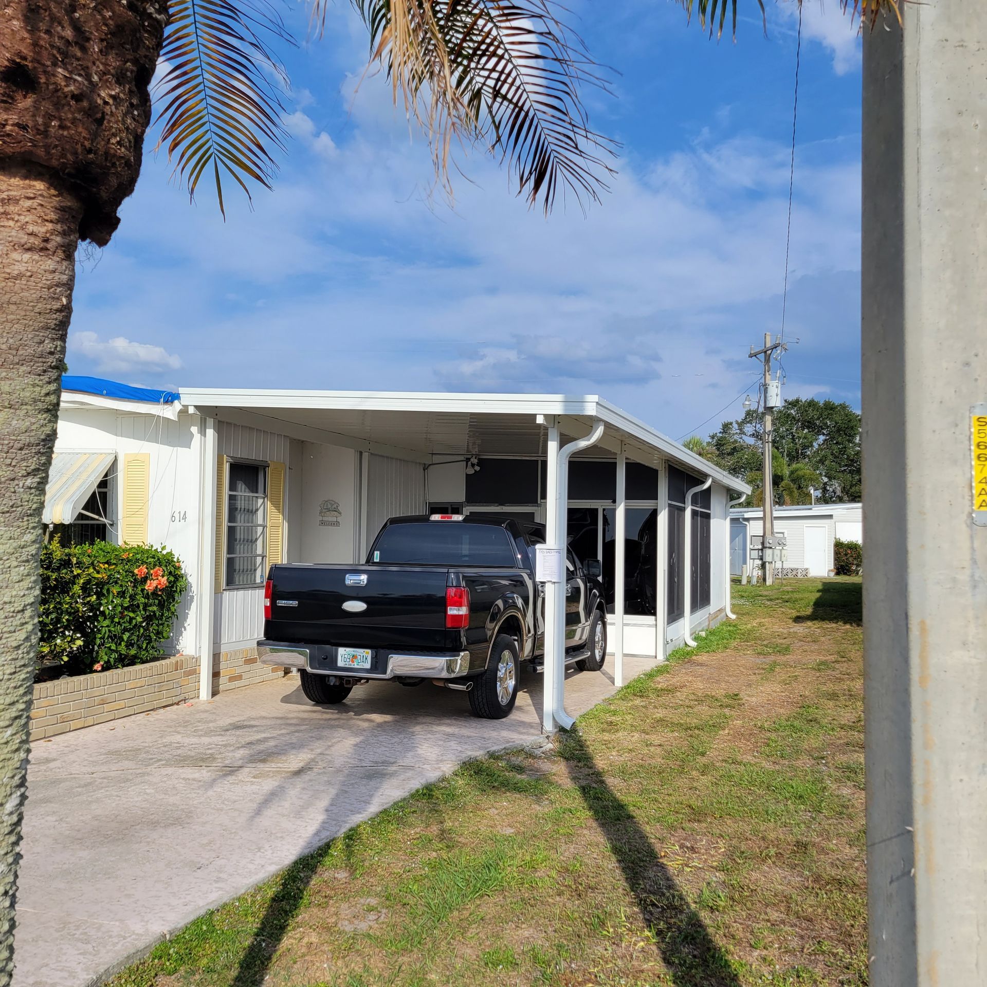 A black truck is parked under a canopy in front of a mobile home