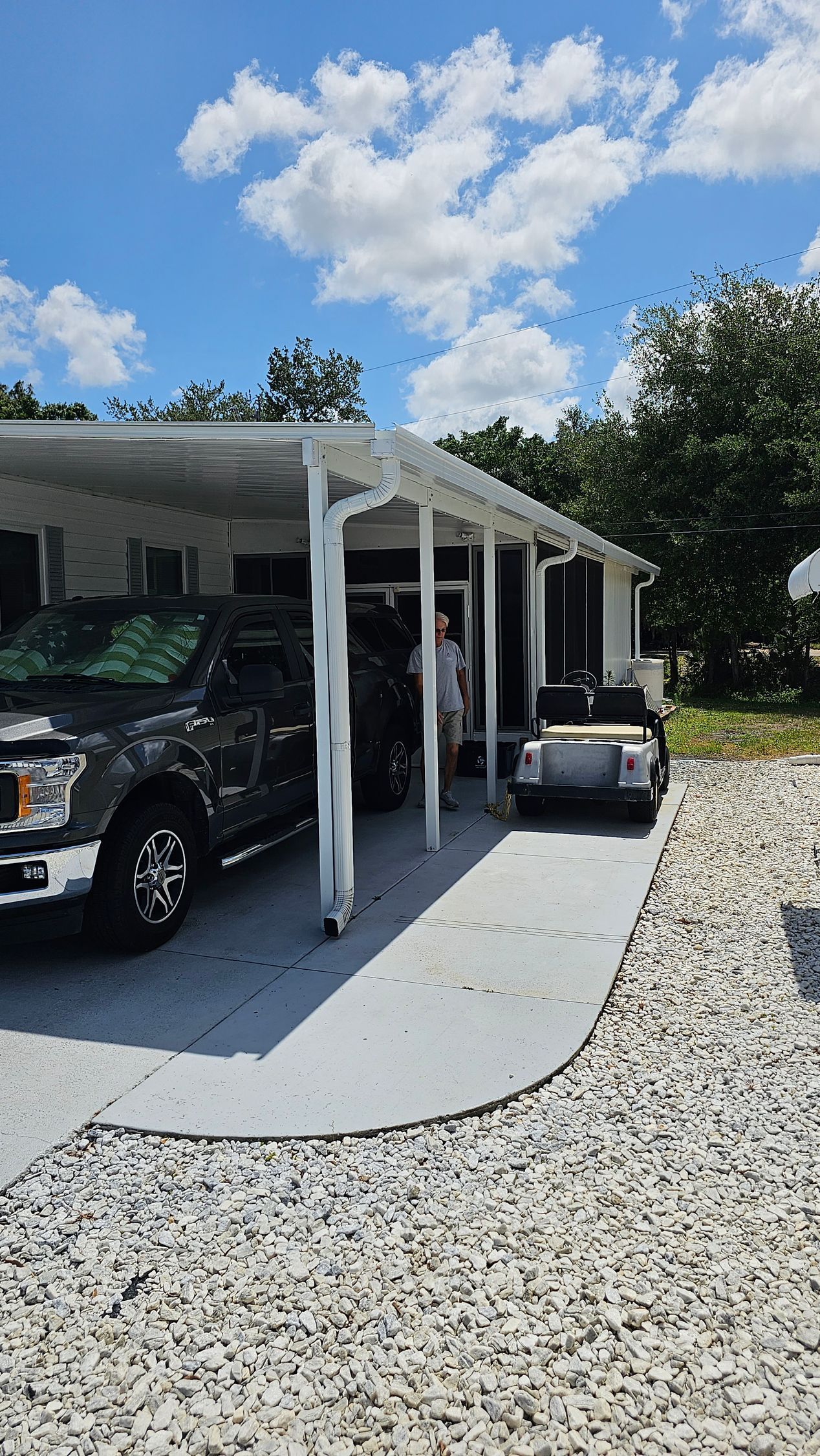 A truck is parked under a canopy in front of a house.