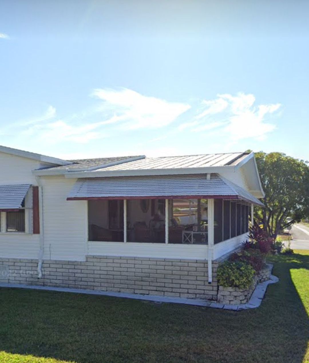 A white mobile home with a screened in porch and a brick wall.