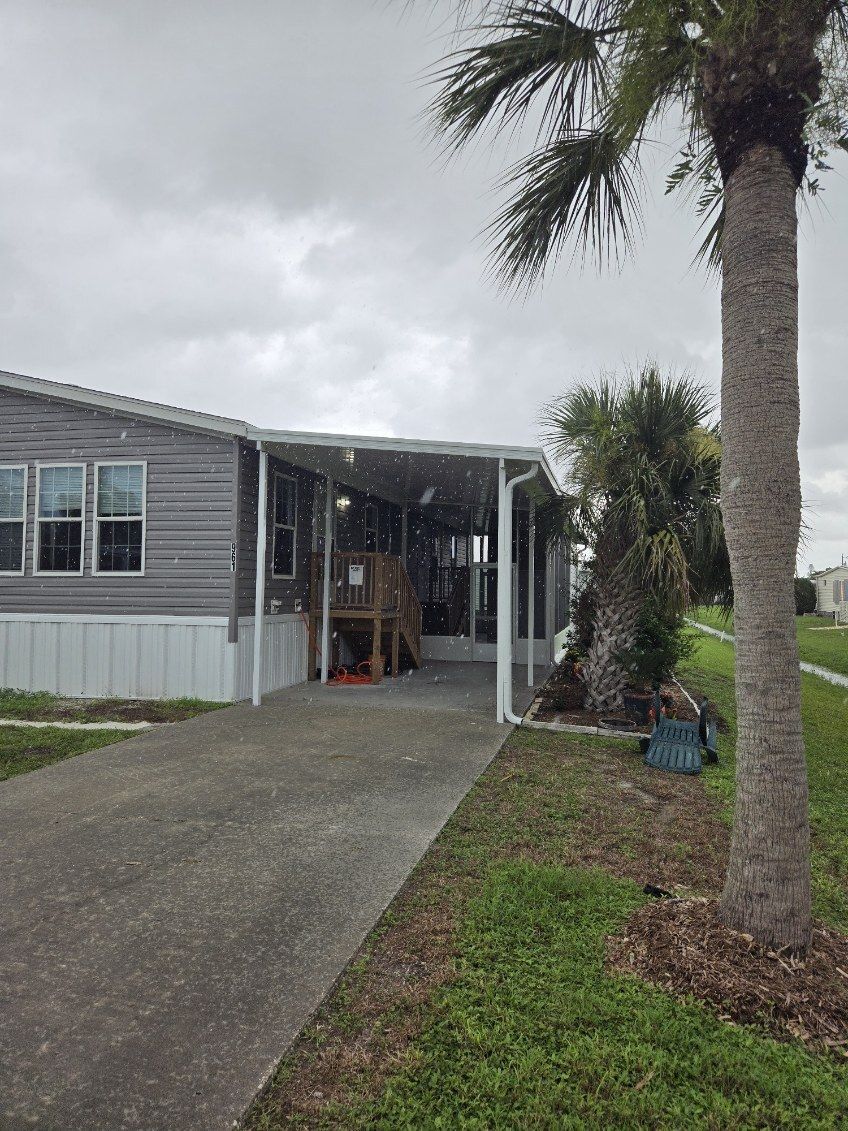 A mobile home with a covered driveway and a palm tree in front of it.