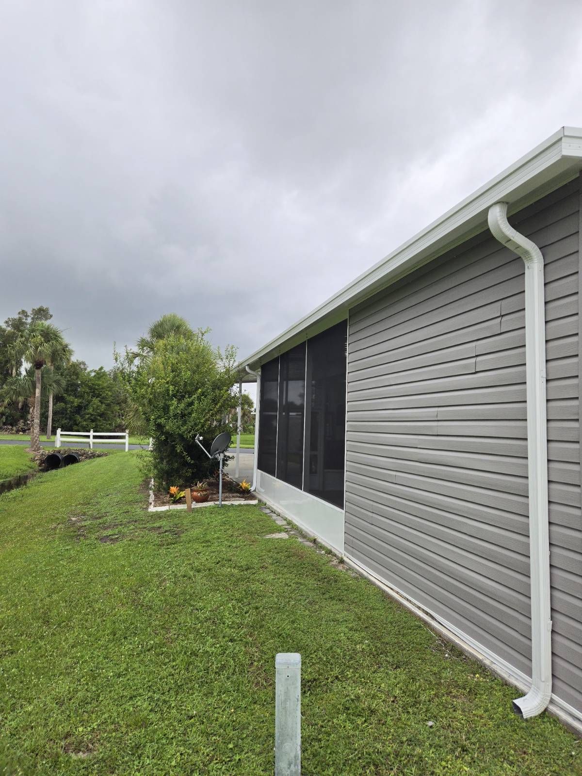 A mobile home with a screened in porch and a gutter on the side of it.