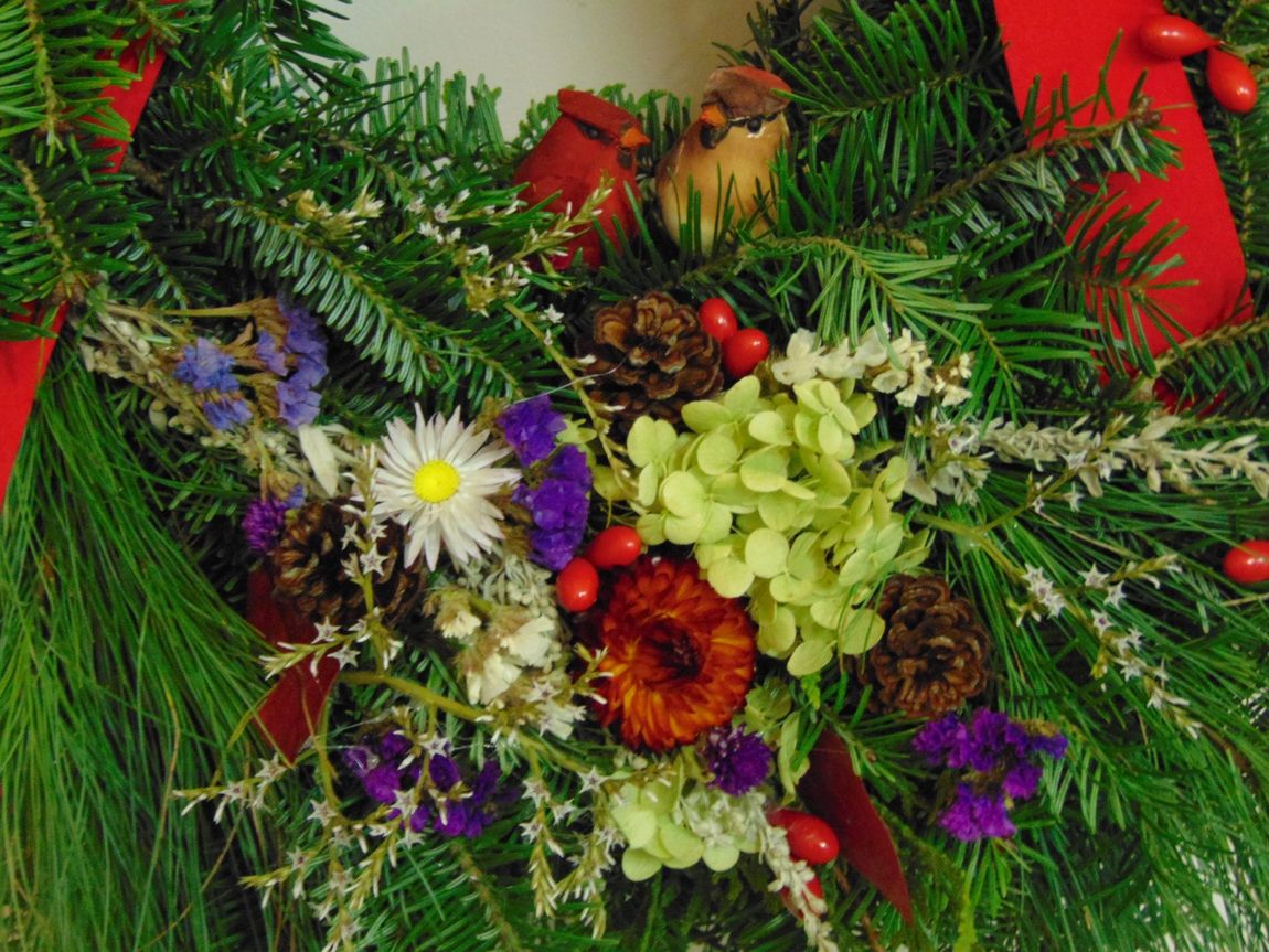 A close up of the flowers, sprigs, and pinecones on a wreath