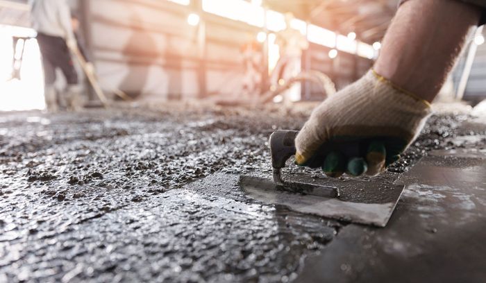 Person in gloves using a trowel to smooth wet concrete.