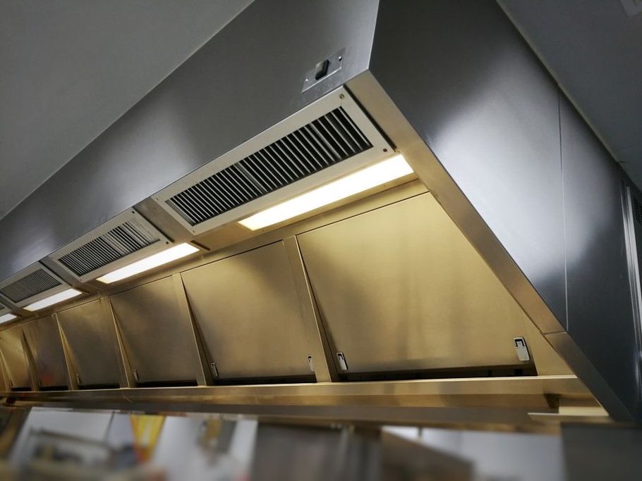 Stainless steel kitchen hood with vents and lights above a row of countertop sneeze guards