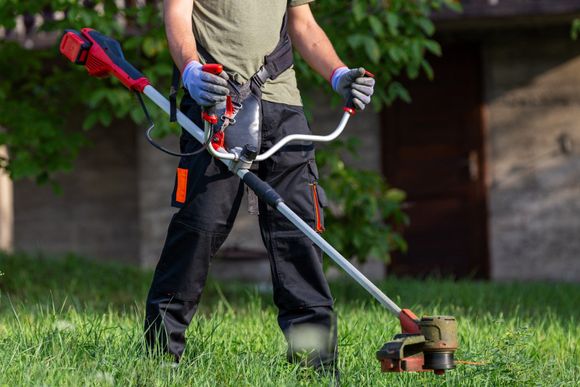 A picture of a man using a string trimmer on a lawn.