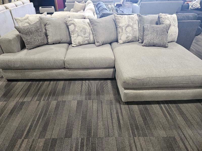 Gray sectional sofa with patterned pillows on a gray patterned rug.