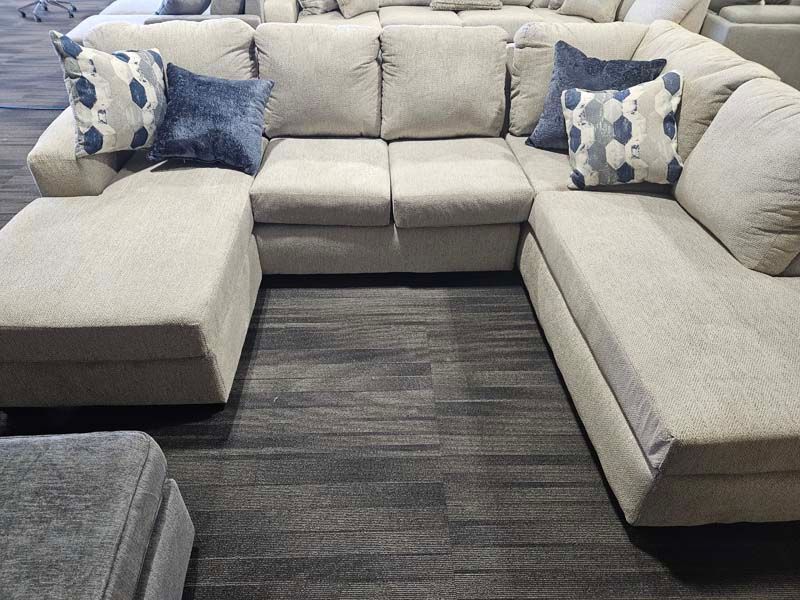 U-shaped beige sectional sofa with blue patterned pillows, set on dark carpet.