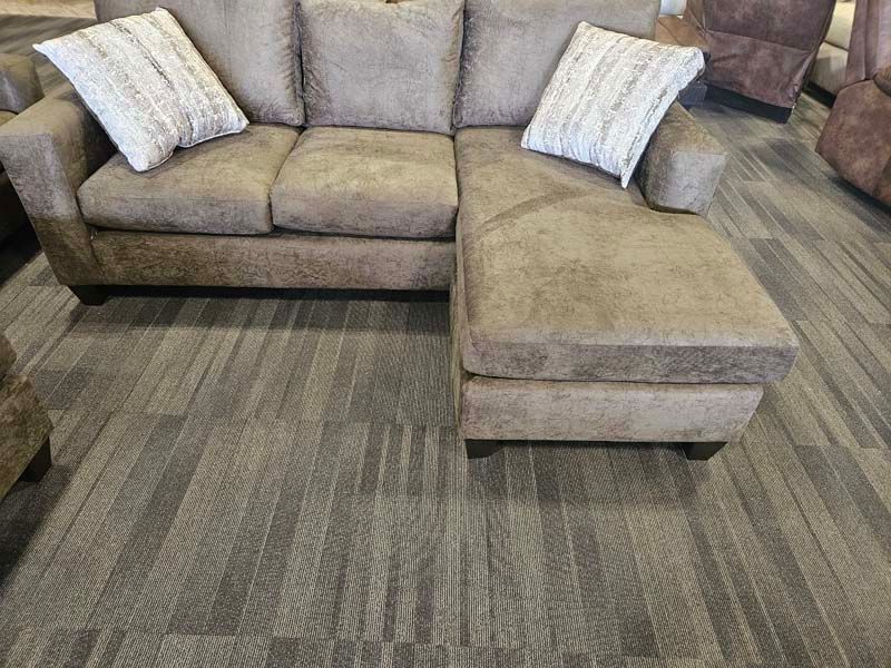 Brown sectional sofa with two white throw pillows on a patterned gray floor.