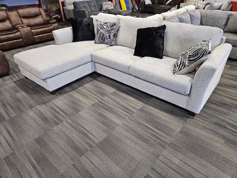 Light gray sectional sofa with black and patterned pillows on gray patterned carpet.