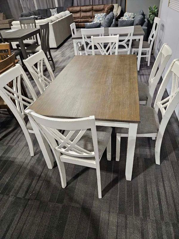 Dining table set with white chairs, gray seats, and a brown tabletop in a showroom.