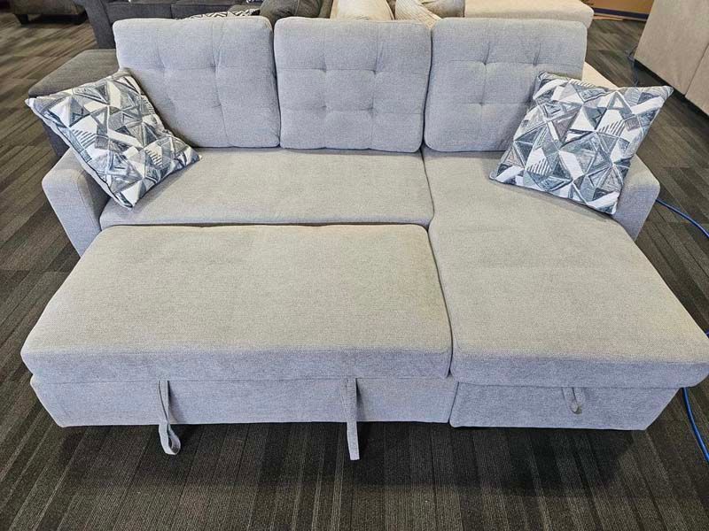 Gray sectional sofa with pull-out bed and two decorative pillows on display in a store.