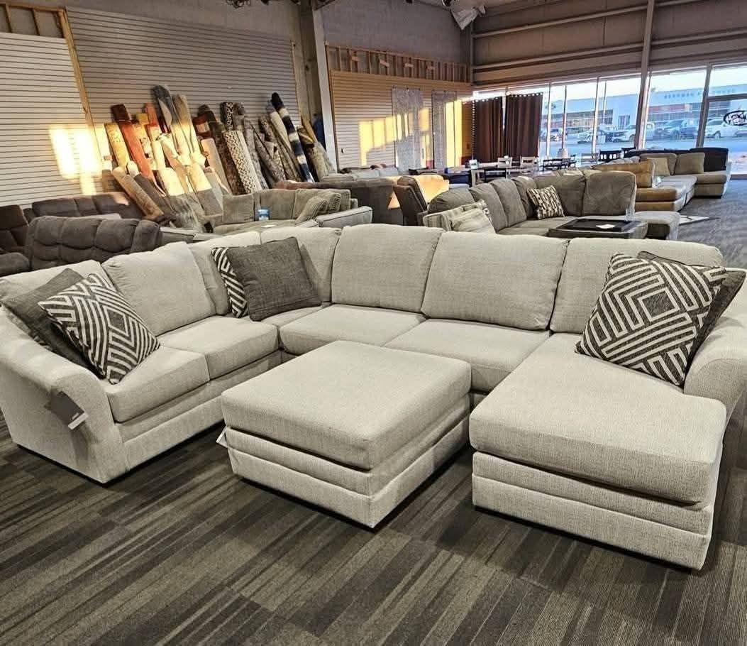Living room with open kitchen, featuring a light-colored sofa, green chairs, and wooden cabinets.